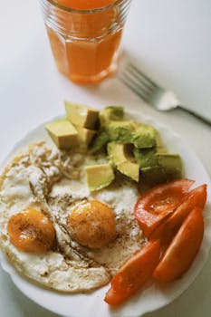 Plate of fried eggs with avocado and tomatoes, perfect for a nutritious breakfast.