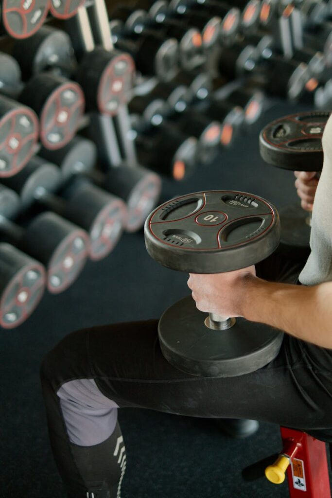 About A person lifting dumbbells while sitting on a bench in a modern gym setting.