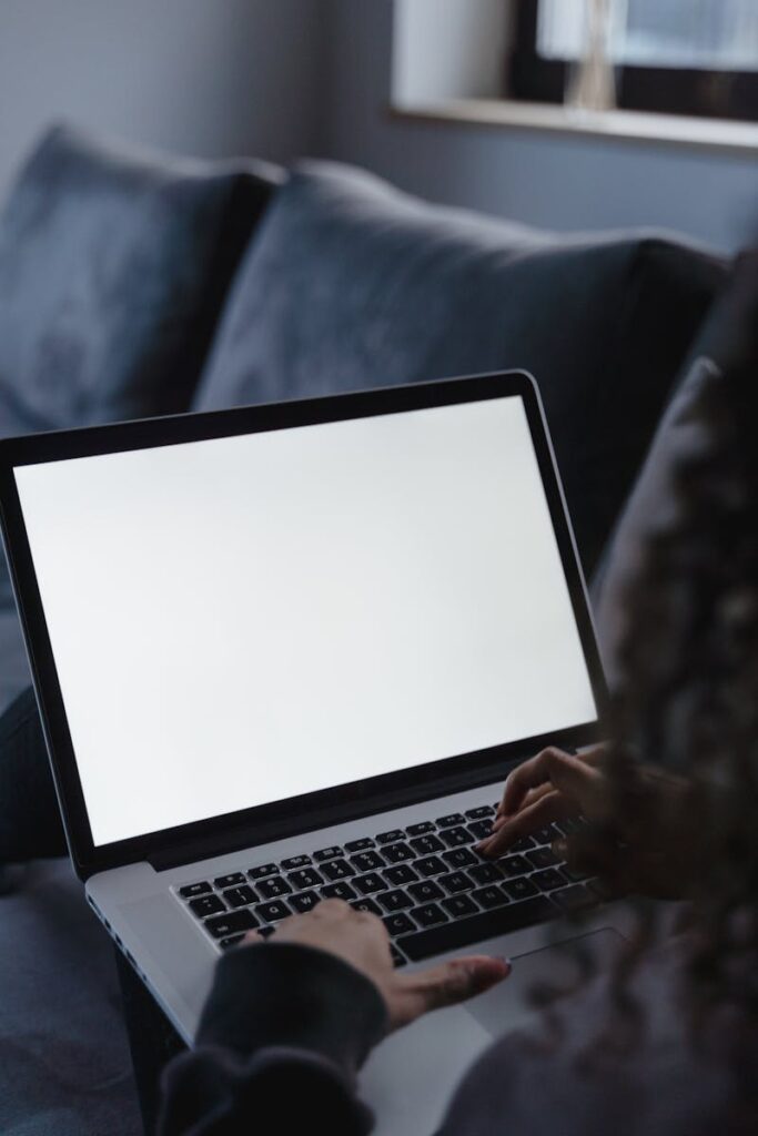 A woman uses a laptop with a blank screen while sitting on a sofa in a cozy room.