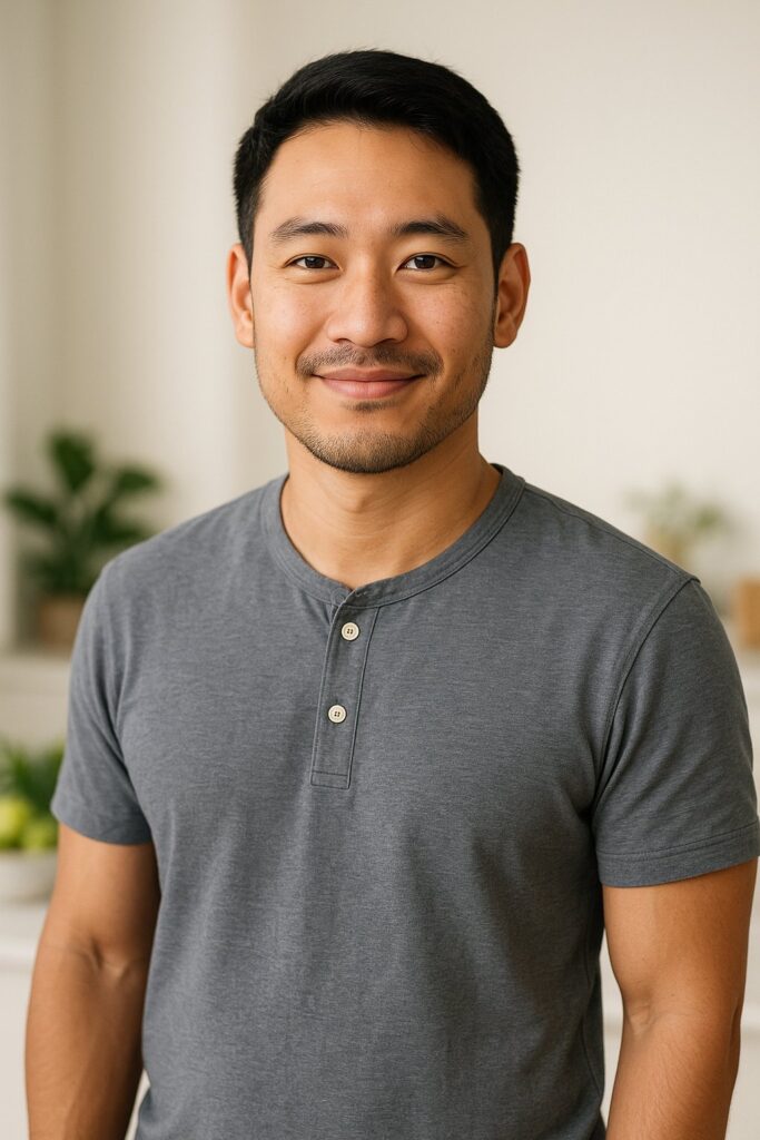 A clean, professional lifestyle portrait of an Asian man in his late 20s to early 30s, standing in soft natural lighting with a neutral light background. Friendly smile, relaxed posture, wearing casual but tidy clothing (plain fitted T-shirt or casual button-up). The atmosphere should feel trustworthy, calm, and wellness-focused — subtle hints of a healthy lifestyle, such as soft greens or blurred kitchen/fitness elements in the background. High-resolution, editorial-quality portrait that conveys approachability, clarity, and credibility.